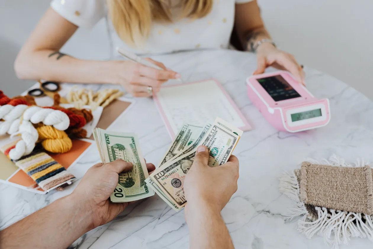 Two people counting cash and using a calculator while budgeting at a table