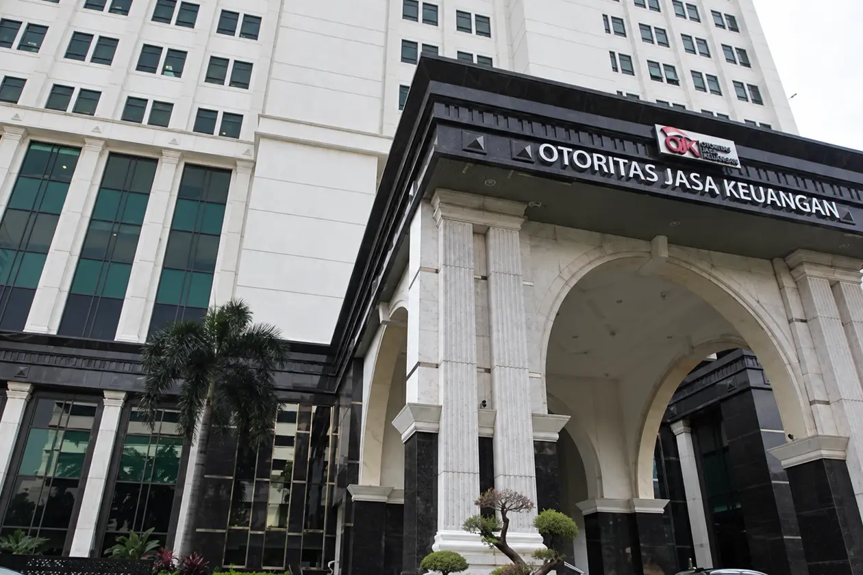 The Otoritas Jasa Keuangan (OJK) office tower in Jakarta with its arched entrance and OTORITAS JASA KEUANGAN signage, seen from ground level