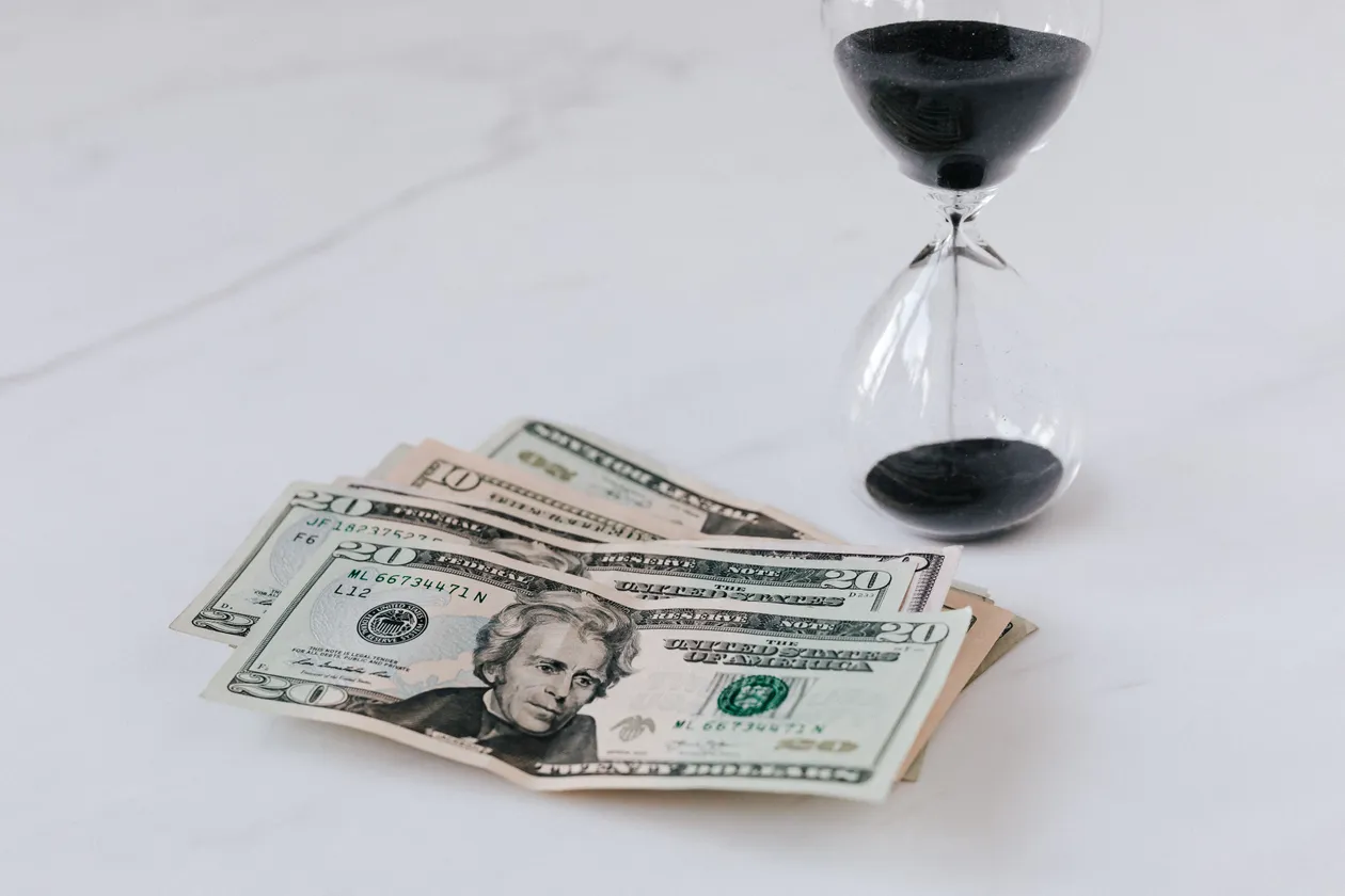 Hourglass resting on a heap of United States dollar bills