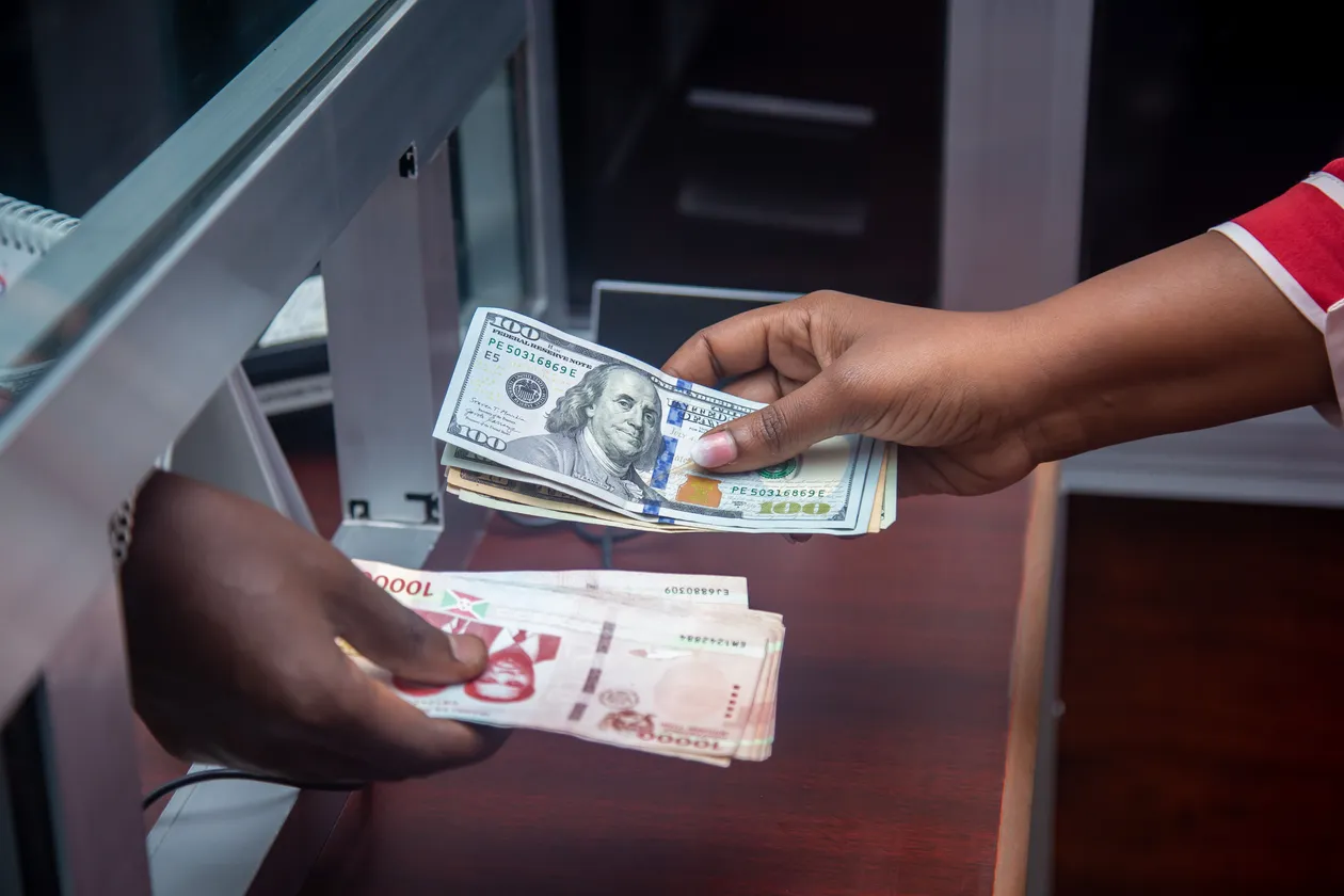 Two hands exchanging bundles of U.S. dollar and Indonesian rupiah banknotes across a counter
