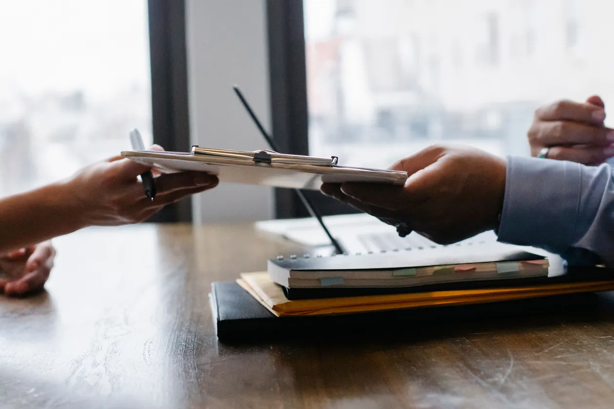 Cropped view of a job candidate handing a document across a wooden desk to another person in business attire