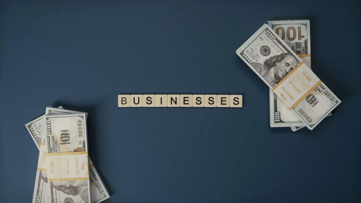 Letter tiles spelling a word beside stacked 100 dollar bills representing funding