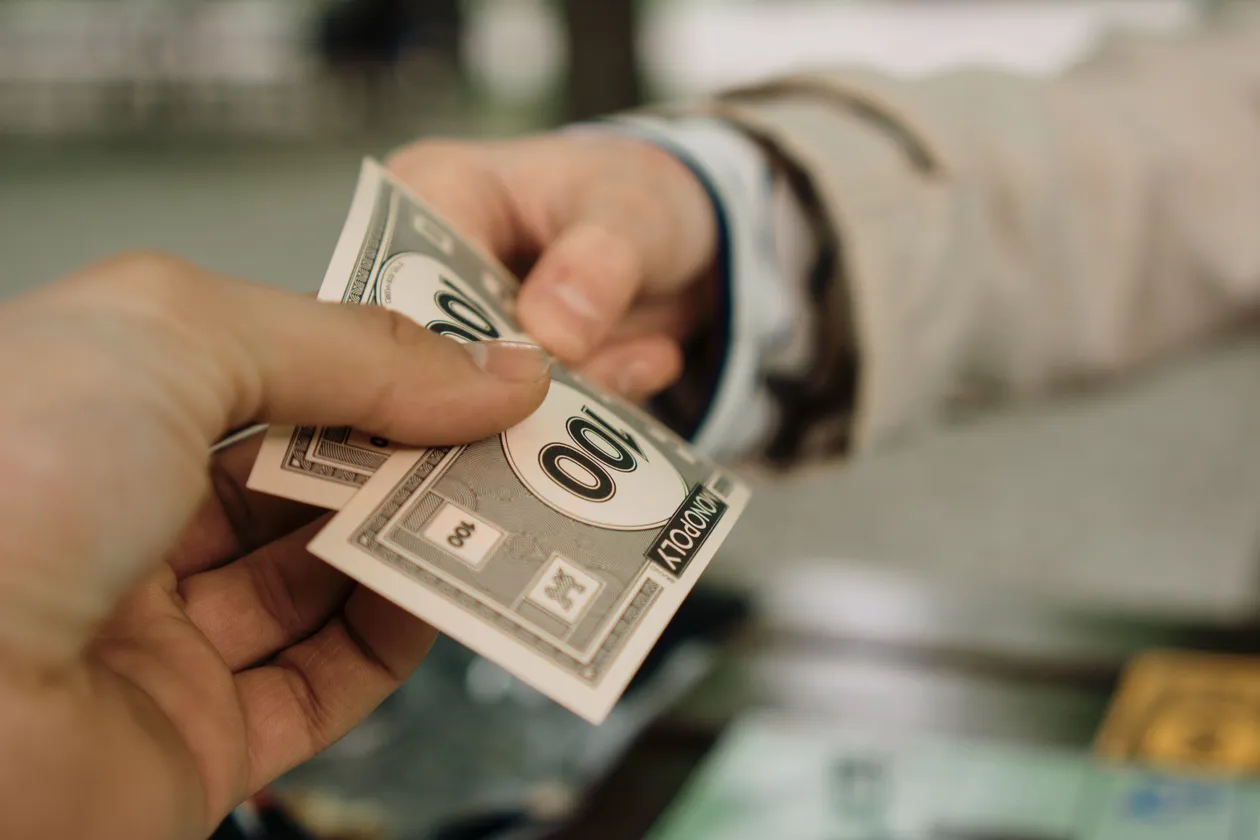 Two hands exchanging Monopoly money bills